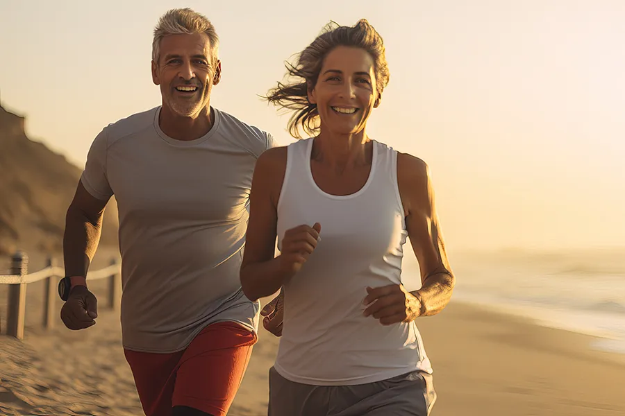 Retatrutide-Clinic A fit older couple happily jog on the beach at sunset. Get Retatrutide for weight loss from Camp Beauty and Wellness.